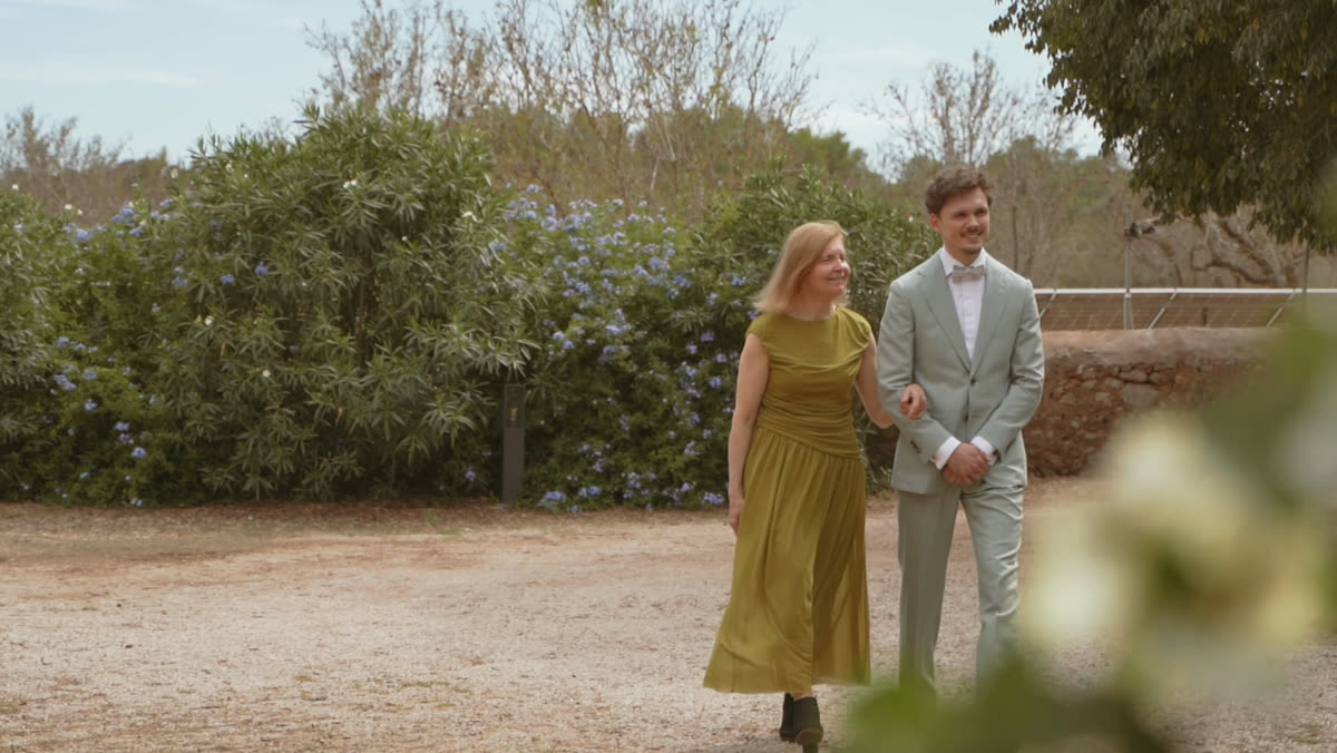 Bräutigam geht mit einer Frau im olivgrünen Kleid über einen sandigen Hof auf Mallorca.